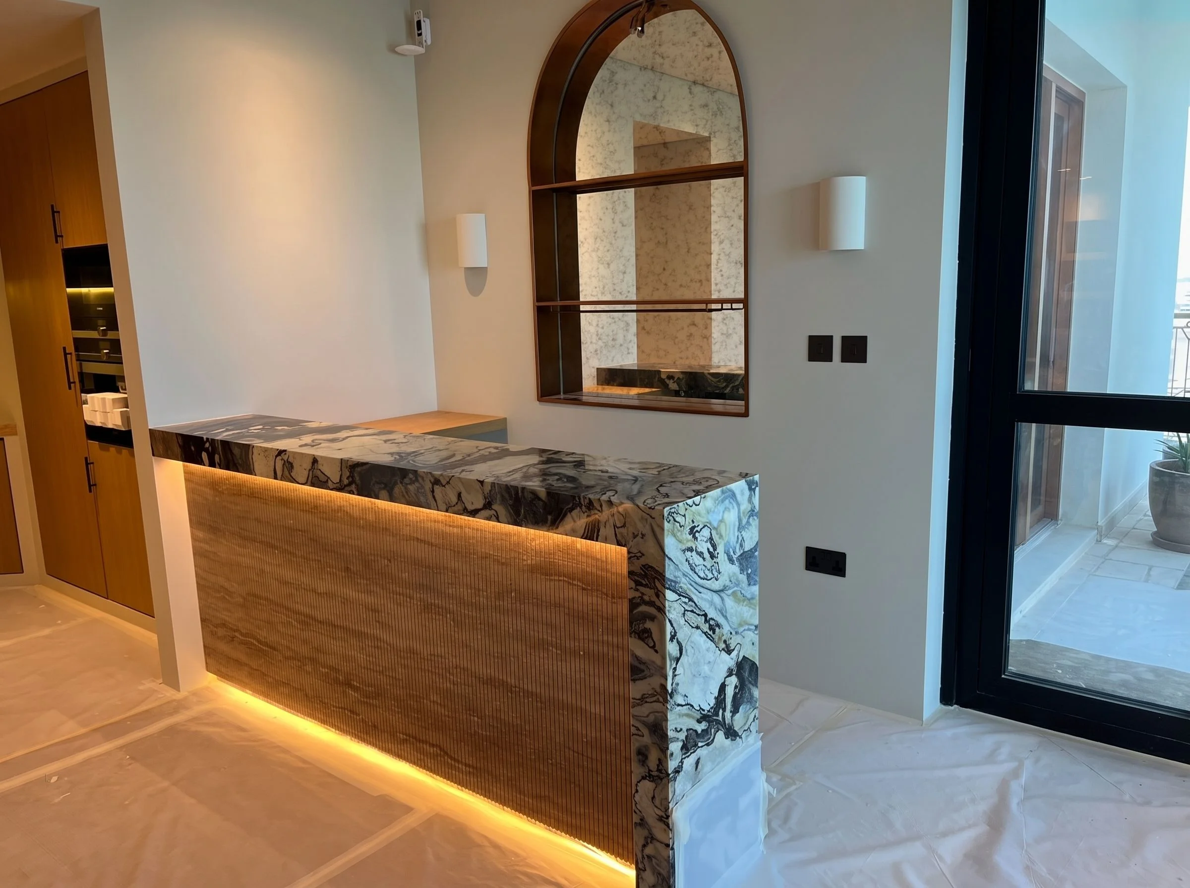 Dubai Marina apartment: Stone-topped bar counter with a fluted, backlit front and an arched mirror niche